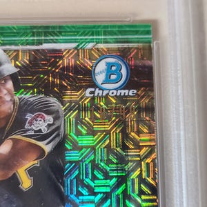 Puede incluir: Una tarjeta de b&eacute;isbol con un jugador con el uniforme de los Piratas de Pittsburgh. La tarjeta tiene un fondo hologr&aacute;fico verde y dorado con la palabra "Chrome" y el logotipo de Bowman. El jugador lleva un casco negro.