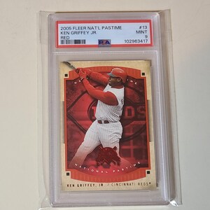 May include: A baseball trading card of Ken Griffey Jr. in a red and white Cincinnati Reds uniform, swinging a bat. The card is from the 2005 Fleer Nat'l Pastime series and is graded as Mint 9. The card is encased in a protective plastic sleeve.