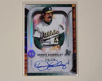 Peut inclure: Une carte de baseball représentant Dennis Eckersley, un ancien lanceur de la Major League Baseball. La carte est une édition autographiée certifiée Topps et est numérotée 158/175. Eckersley porte un uniforme des Athletics d'Oakland vert et or et tient un gant de baseball. La carte a un fond argenté et bleu avec une bordure en bois.