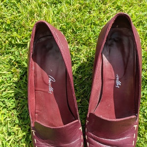 May include: A pair of burgundy leather loafers with white stitching. The loafers have a pointed toe and a low heel. The inside of the loafers is labeled "Cavalli".