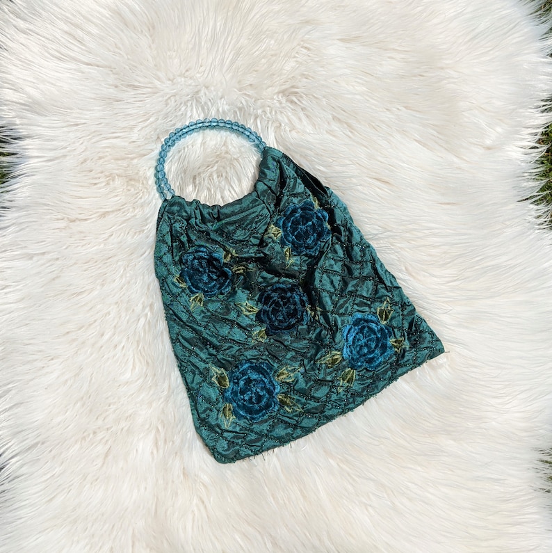 Pode incluir: Uma bolsa acolchoada azul turquesa com al&ccedil;a de contas e detalhes florais bordados. As flores s&atilde;o de um azul mais escuro.