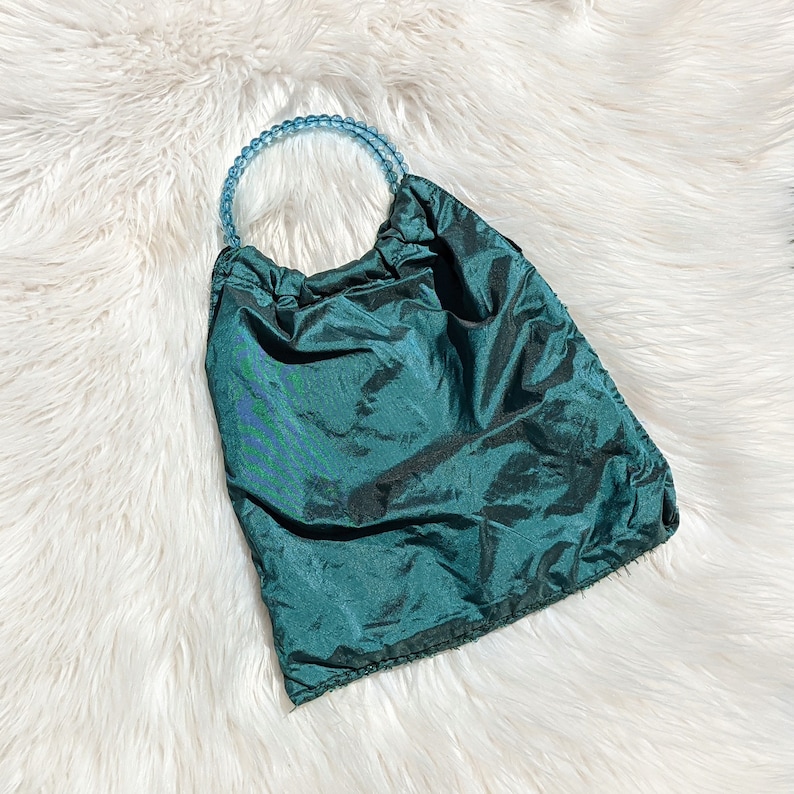 Pode incluir: Uma bolsa de m&atilde;o de tecido azul-esverdeado com uma al&ccedil;a de contas azul claro.