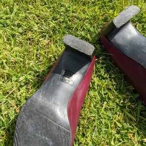 May include: A pair of burgundy heeled shoes with black soles. The shoes have a size label on the sole that reads "4 1/2 37".