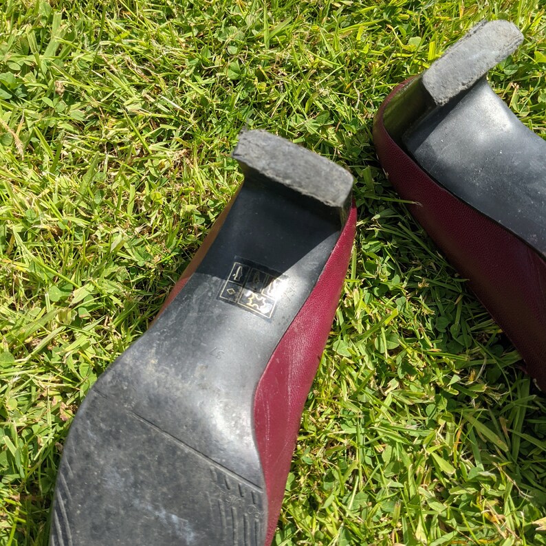 May include: A pair of burgundy heeled shoes with black soles. The shoes have a size label on the sole that reads "4 1/2 37".