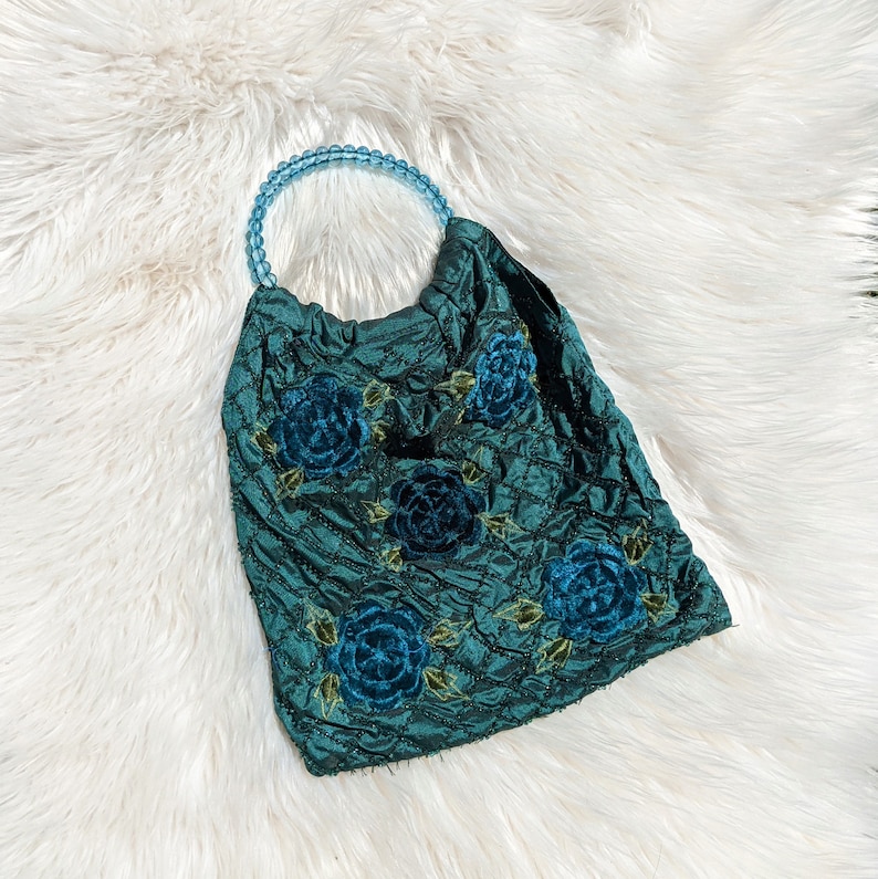 Pode incluir: Uma bolsa acolchoada azul-esverdeada com uma al&ccedil;a de contas e rosas de veludo azul bordadas.