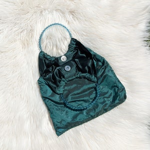 Pode incluir: Uma bolsa de m&atilde;o de cetim azul-esverdeado com uma al&ccedil;a de contas. A bolsa tem um design franzido e um fecho de aba.