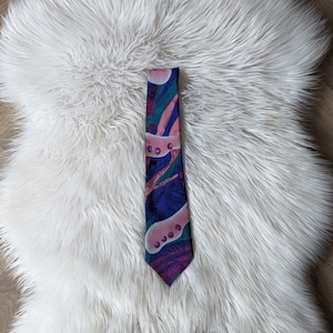 May include: A patterned tie with a blue, pink and green abstract design. The tie has a white background with pink and green circles.