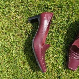 May include: A pair of burgundy leather heeled shoes with white stitching. The shoes have a pointed toe and a low heel.