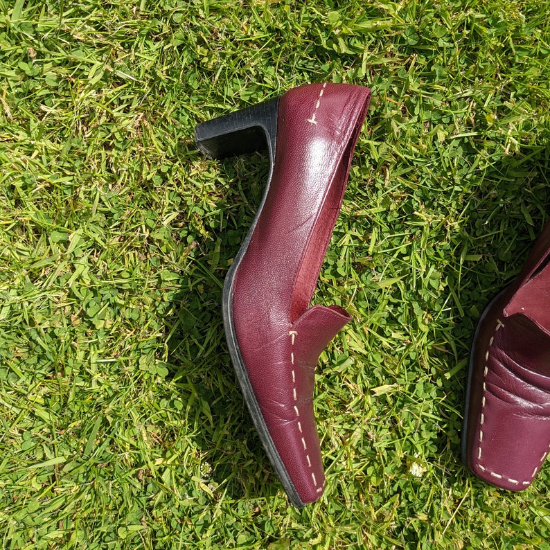 May include: A pair of burgundy leather heeled shoes with white stitching. The shoes have a pointed toe and a low heel.