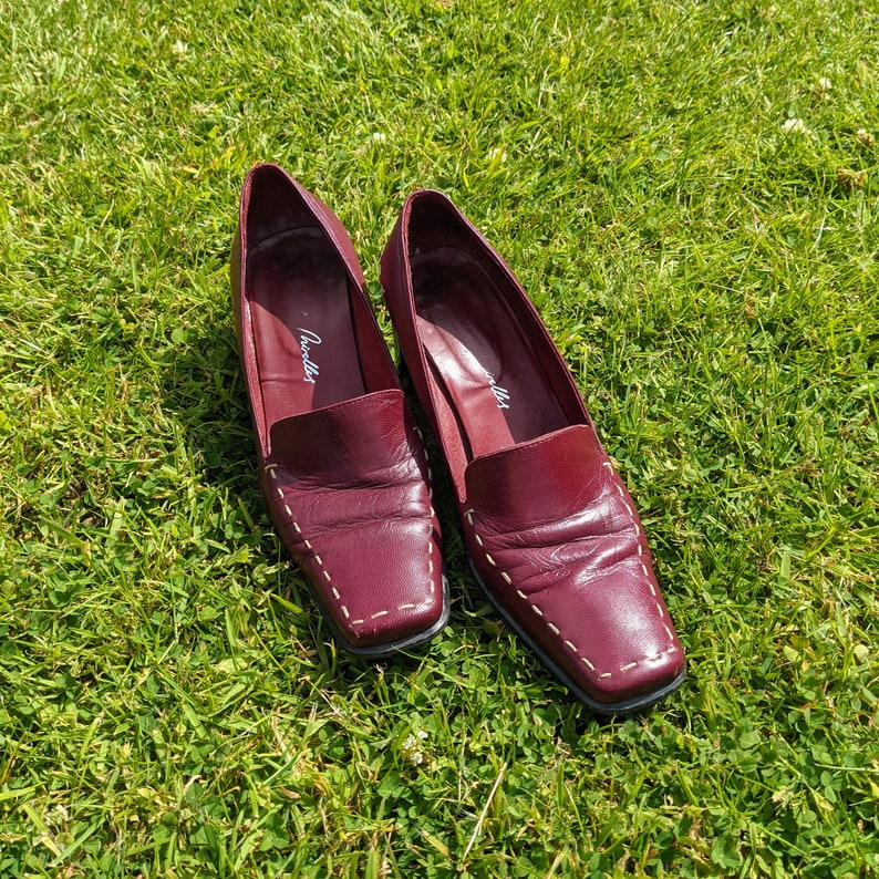 May include: A pair of burgundy leather loafers with white stitching. The loafers have a square toe and a low heel. The brand name "Giulietta" is visible on the inside of each shoe.