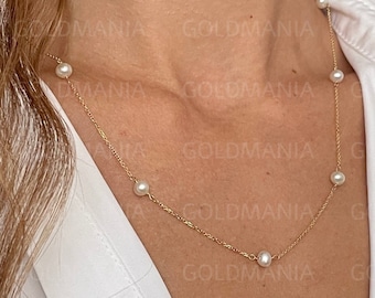 Puede incluir: Un delicado collar de cadena de oro con pequeñas perlas blancas. El collar lo lleva una persona con el pelo largo y castaño.