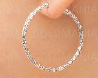 May include: Silver hoop earrings with a braided design. The earrings are worn in a person's ear.
