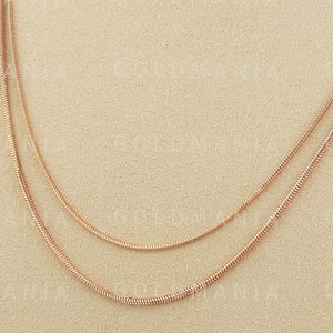 May include: A rose gold chain necklace with three strands of varying lengths. The necklace is displayed on a beige mannequin bust.