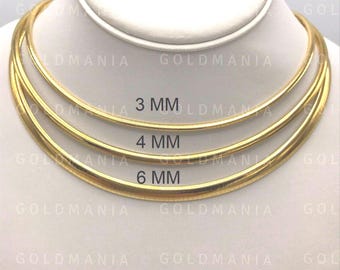Puede incluir: Tres collares omega dorados de 3 mm, 4 mm y 6 mm de grosor, exhibidos sobre un busto blanco. Los collares son lisos y brillantes. El nombre de la marca "GOLDMANIA" es visible en el fondo.