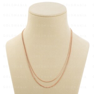 May include: A three-strand rose gold necklace on a white mannequin bust. The necklace is made of thin, delicate chains.