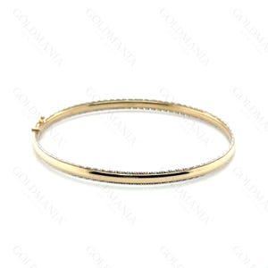 May include: A gold bangle bracelet with a textured border and a clasp closure. The bracelet is a simple, elegant design, perfect for everyday wear. The bangle is approximately 2.5 inches in diameter.