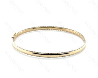 May include: A gold bangle bracelet with a textured border and a clasp closure. The bracelet is a simple, elegant design, perfect for everyday wear. The bangle is approximately 2.5 inches in diameter.