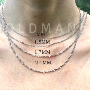 Puede incluir: Primer plano de cuatro collares de cadena de cuerda plateados de diferentes grosores: 1 mm, 1,5 mm, 1,7 mm y 2,1 mm. Los collares se muestran en el cuello de una persona, mostrando los diferentes tama&ntilde;os de cadena. El texto "1MM", "1.5MM", "1.7MM" y "2.1MM" es visible.