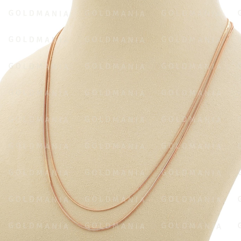 May include: A rose gold chain necklace with three strands of varying lengths. The necklace is displayed on a beige mannequin bust.