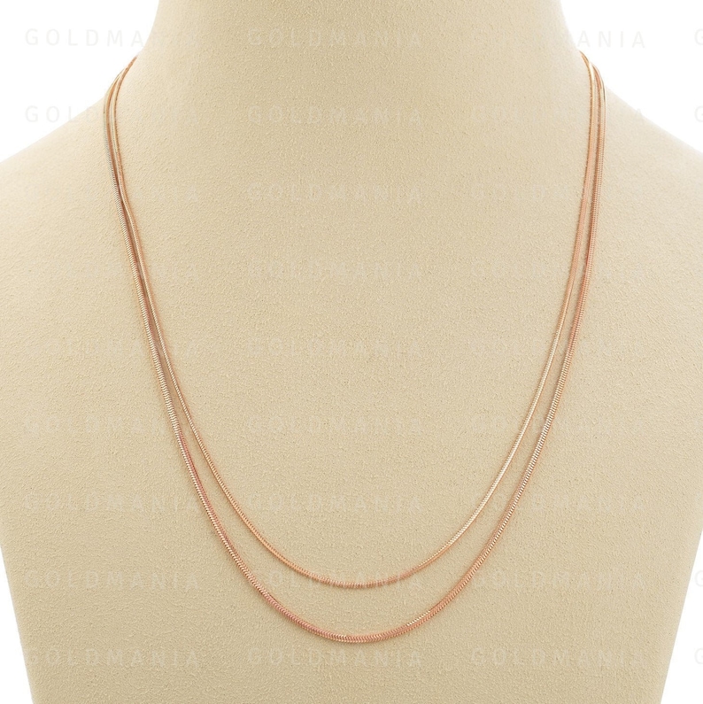 May include: Three gold chains of different lengths and widths, layered on a beige mannequin bust.