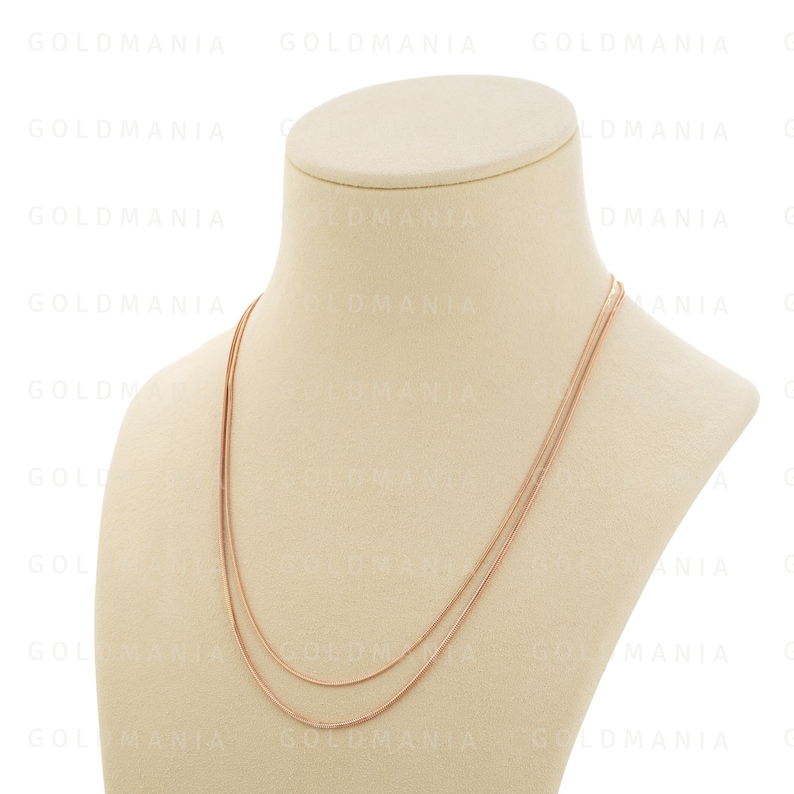 May include: A rose gold chain necklace on a white mannequin. The necklace is made of two thin chains, one slightly thicker than the other.