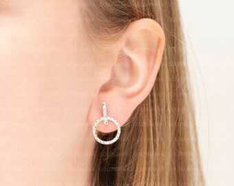 May include: Silver earrings with a small circle design and a vertical bar. The earrings are shown on a person's ear.