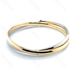 Puede incluir: Una pulsera de brazalete de dos tonos. La pulsera presenta una banda dorada entrelazada con una banda plateada. La pulsera tiene un cierre de broche y está sobre un fondo blanco. Joyería.