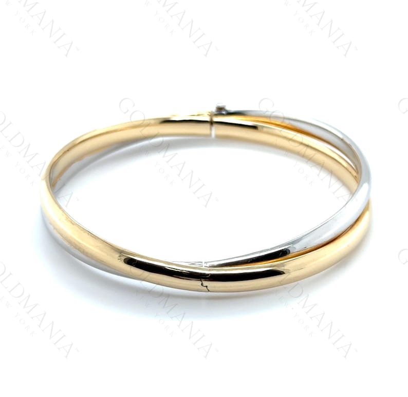 May include: A two-tone bangle bracelet. The bracelet features a gold-colored band intertwined with a silver-colored band. The bracelet has a clasp closure and is set against a white background. Jewelry.