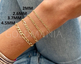 May include: Four gold-toned figaro chain bracelets displayed on a wrist, labeled with widths of 2mm, 2.6mm, 3.7mm, and 4.5mm. The chains feature a repeating pattern of one elongated oval link followed by three smaller circular links in a polished finish.