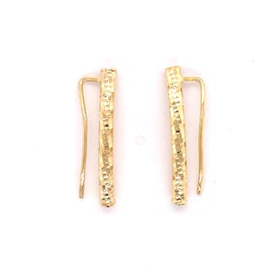 May include: A pair of gold earrings with a hammered texture. The earrings are shaped like a long, thin rectangle with a curved hook.