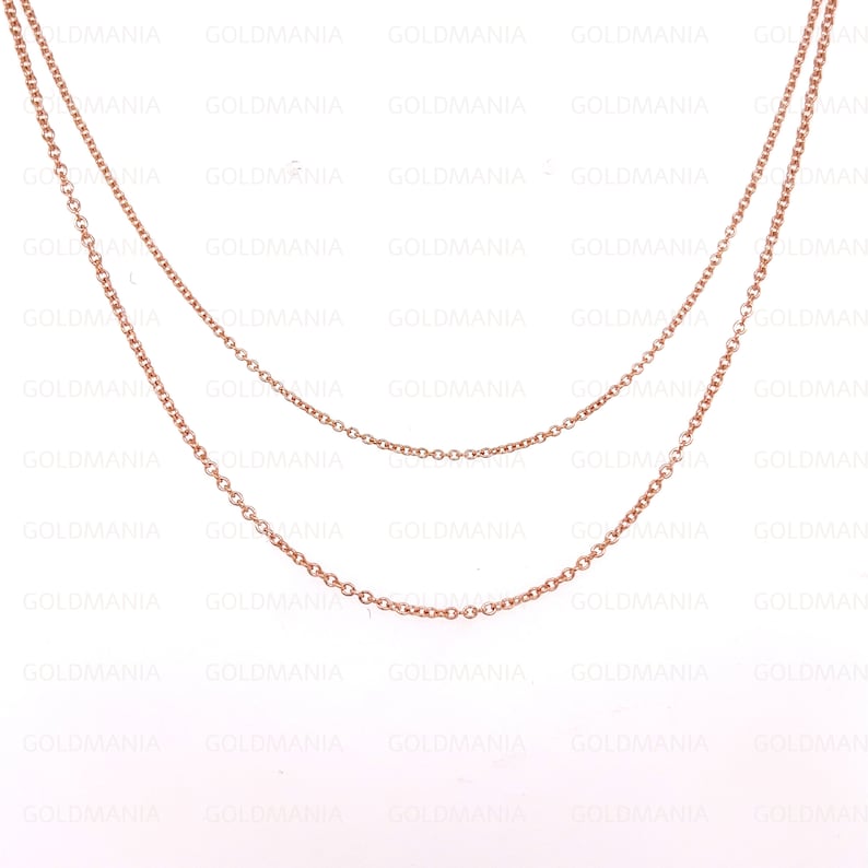 May include: Two delicate rose gold chains, one slightly longer than the other, are layered together. The chains are made of small, round links and are perfect for layering with other necklaces.