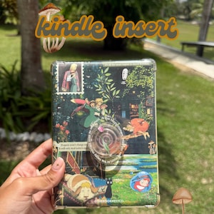 May include: Clear Kindle insert with a colorful design featuring anime characters and the text "kindle insert". The insert has a pop-up grip and is decorated with images of nature and characters.