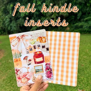 Puede incluir: Dos fundas para Kindle con diseños otoñales. Una funda presenta un collage con una cesta de picnic, setas y un tarro de fresas. La otra funda tiene un patrón de cuadros naranja y blanco. Se muestra el texto "fall kindle inserts".