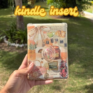 May include: A Kindle insert with an autumn-themed design. The insert features a collage of fall elements, including a bow, teacup, cat, basket, and jar of roses. The text "kindle insert" is in a cursive font.
