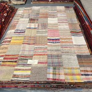 Op de afbeelding: Een patchwork tapijt gemaakt van verschillende kleurrijke stoffen, met een label met de tekst "303 216 x 305 CHMAT".