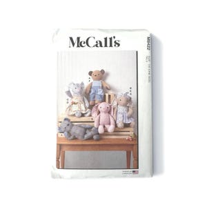 May include: McCall's sewing pattern featuring stuffed animal designs. The pattern includes instructions for creating a bear, bunny, elephant, and other plush toys. The toys are displayed on a wooden bench. The pattern is printed in the USA.