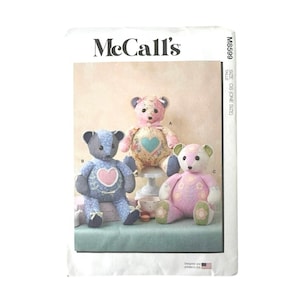 May include: A McCall's M8599 sewing pattern envelope featuring three stuffed teddy bears. The bears are crafted from various floral and patterned fabrics in shades of blue, pink, and cream, each decorated with heart or flower appliques.