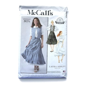 May include: A McCall's sewing pattern envelope for a vintage 80s Laura Ashley style outfit. The front displays a blue floral vest and tiered skirt, with illustrations of two additional garment variations, size A (8-10-12-14-16), and text.