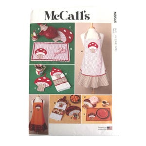 May include: McCall's M8545 sewing pattern envelope featuring kitchen textiles including aprons, placemats, towels, and pot holders. The designs showcase mushroom motifs, polka dots, and striped patterns in red, white, and brown color schemes.