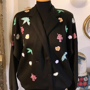 May include: A black double-breasted jacket with a floral embroidered design. The jacket has a relaxed fit and a collar.