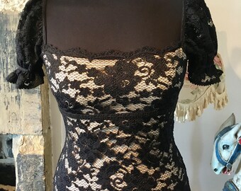 Può includere: Top in pizzo nero con maniche a sbuffo corte e scollo quadrato. Il top è trasparente e presenta un motivo floreale.