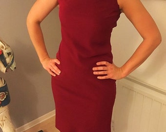 May include: A sleeveless, burgundy dress with a bateau neckline. The dress is fitted and falls to the knees. The model is wearing black tights.