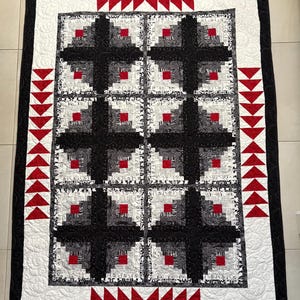 May include: A handmade quilt with a black border and a white center. The quilt features a repeating pattern of black and white squares with red center squares. Red triangle accents are along the edges.