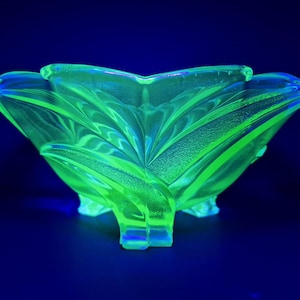 May include: A vibrant green glass bowl with a textured, leaf-like pattern. The bowl has a three-footed base and a scalloped edge. The glass glows against a dark blue backdrop, creating a striking visual effect.