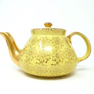 May include: A yellow teapot with a gold floral pattern. The teapot has a round body and a curved spout.