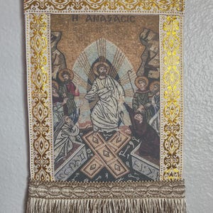 May include: Rectangular tapestry with a religious mosaic scene, featuring figures in robes and halos. The tapestry has gold trim, a decorative border, and a fringe at the bottom. The text "H ANASTACIC" is visible at the top.