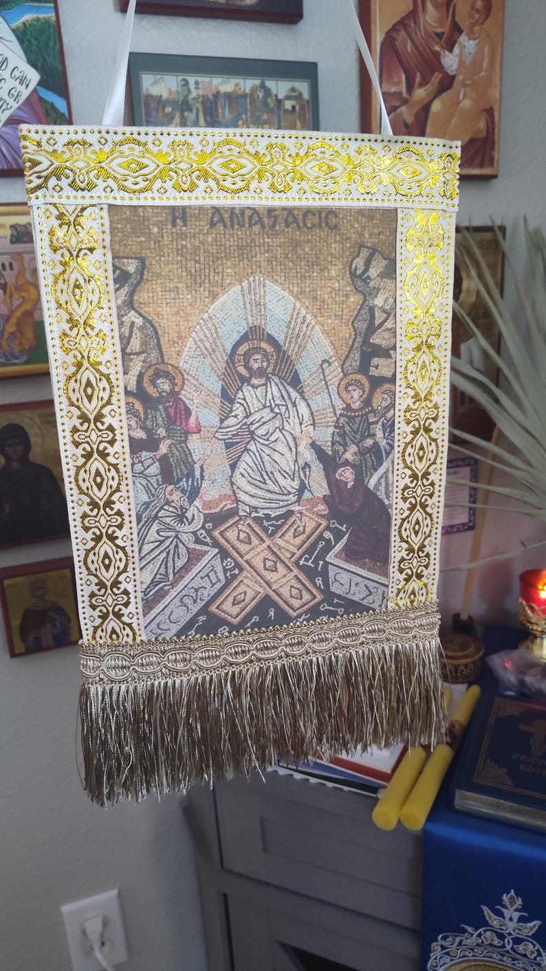 May include: A rectangular religious banner with a mosaic-style image of Jesus Christ surrounded by figures. The banner has a gold and white decorative border with fringe at the bottom. The text "H ANACTACIC" is visible on the banner.