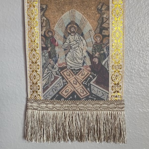 May include: A religious tapestry with a mosaic-style image of Jesus Christ surrounded by figures. The tapestry has gold trim and a fringe at the bottom. The text "H ANAFACIC" is at the top.