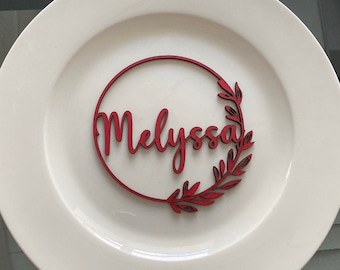 May include: A white plate with a red wooden name card that says "Melyssa" in a cursive font. The name card is in a circle with a leafy design.