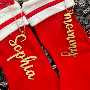 May include: Two red Christmas stockings with white cuffs and gold glitter names. The stockings are decorated with the names "Mommy" and "Sophia".